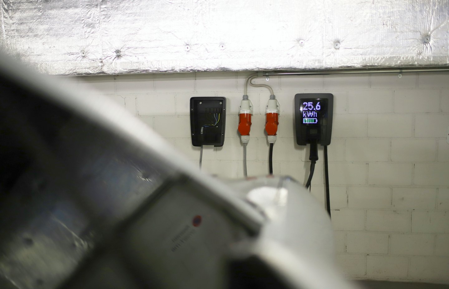 Twee elektrische autoladers tegen een witte bakstenen muur.