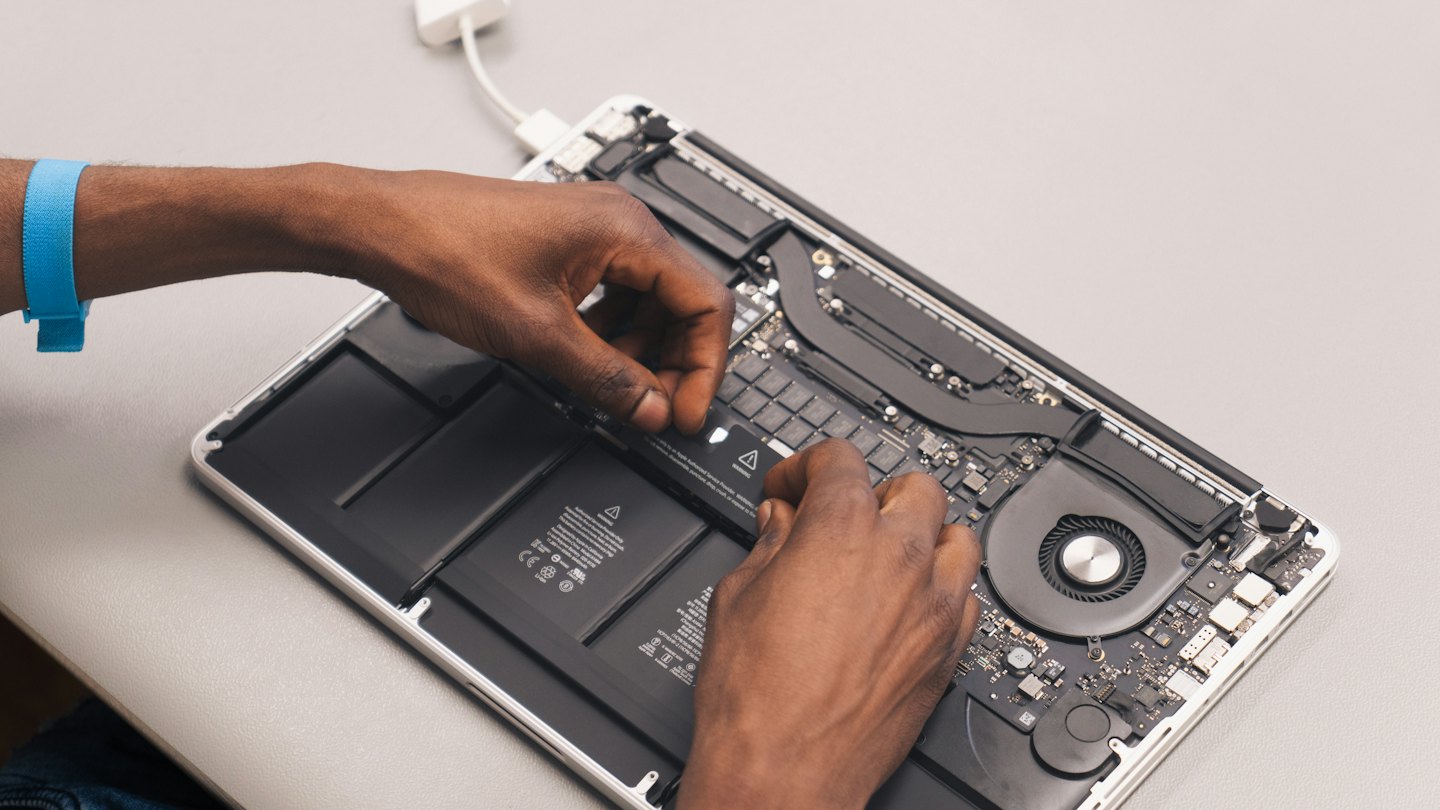 Handen die een open laptop repareren met zichtbare interne componenten.