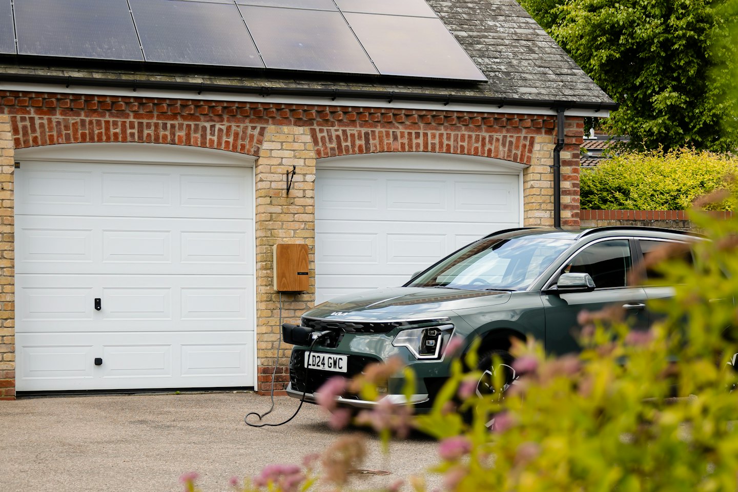 Donkergroene elektrische auto aangesloten op een thuislader.